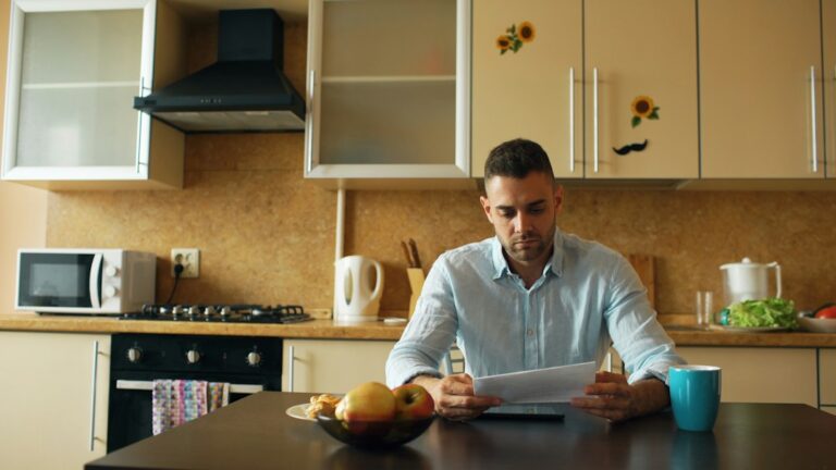 A homeowner reviews credit and insurance documents beside a calculator at a kitchen table.